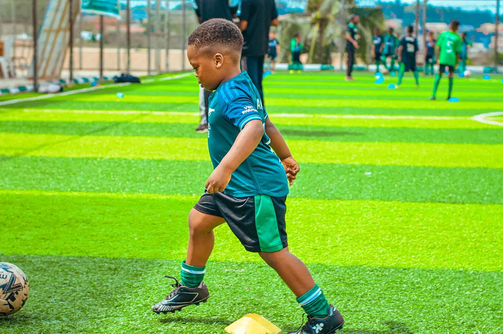 A young player dribbling a football across striped turf